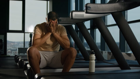 Exhausted man resting after treadmill workout in gym